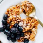 Spoon of delicious oatmeal on a plate of cinnamon roll oatmeal bake with a side of frozen blueberries.