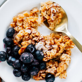 Spoon of delicious oatmeal on a plate of cinnamon roll oatmeal bake with a side of frozen blueberries.