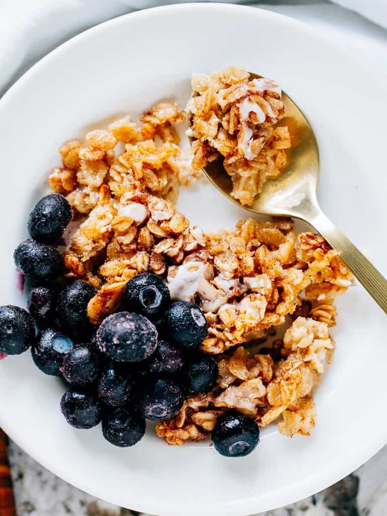 Spoon of delicious oatmeal on a plate of cinnamon roll oatmeal bake with a side of frozen blueberries.