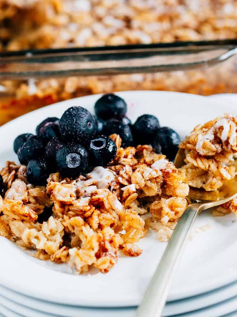 Spoon of delicious oatmeal on a plate of cinnamon roll oatmeal bake with a side of frozen blueberries.