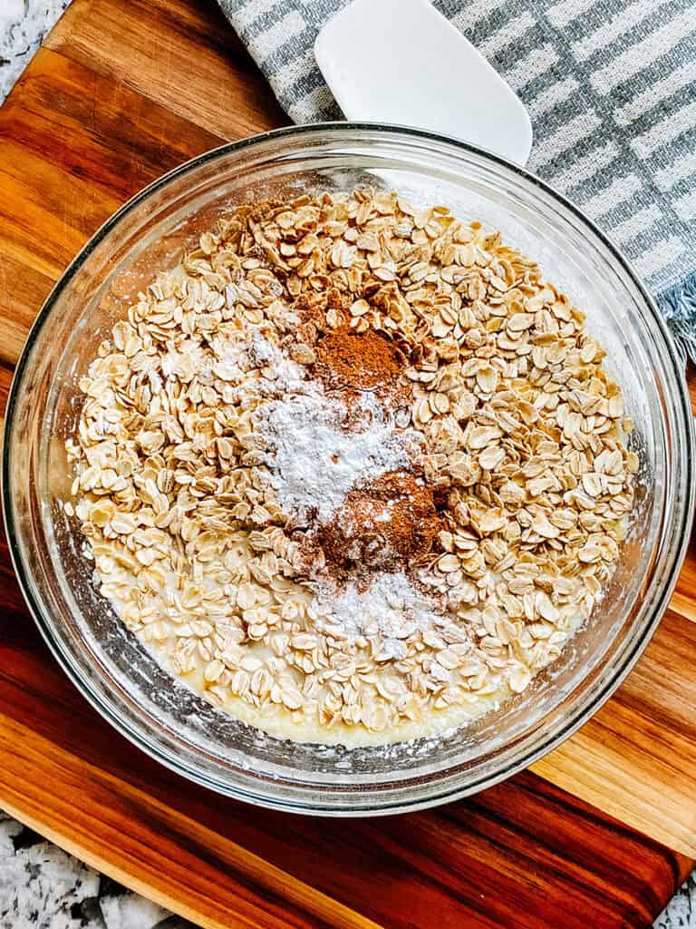 Oats, baking powder, cinnamon, and salt on top of the whisked wet ingredients.