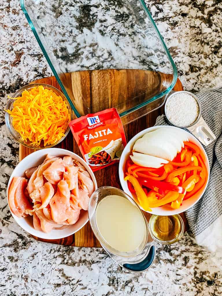 The ingredients for this chicken fajita bake casserole: sliced chicken breasts. sliced bell peppers and onions, oil, chicken broth, rice, shredded cheddar cheese, and fajita seasoning.