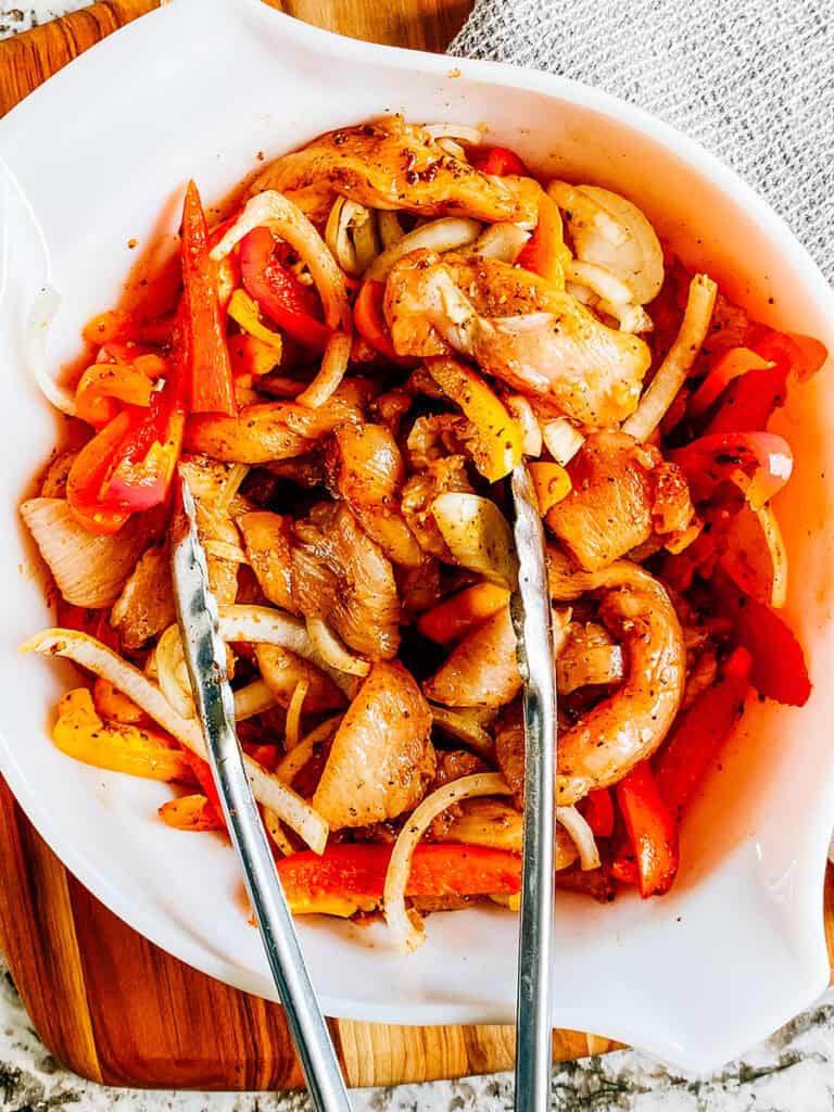 Raw sliced chicken breasts, bell peppers, and onions coated in a oil and fajita seasoning mix.