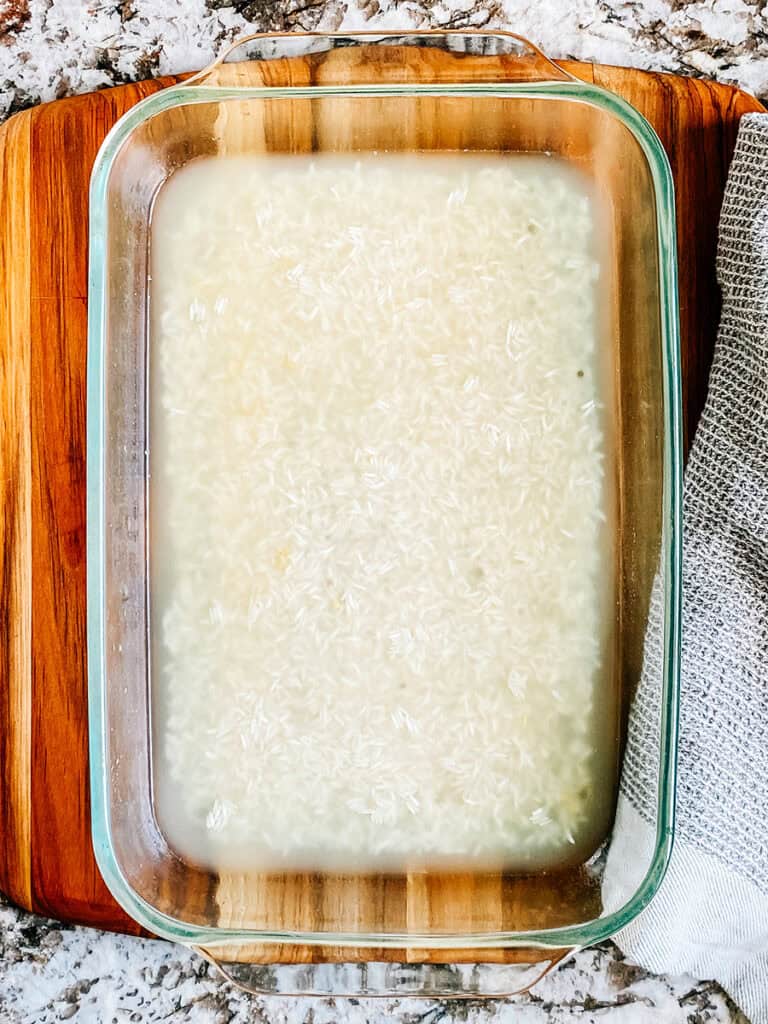 A 9x13 in baking dish with chicken broth and uncooked rice at the bottom.