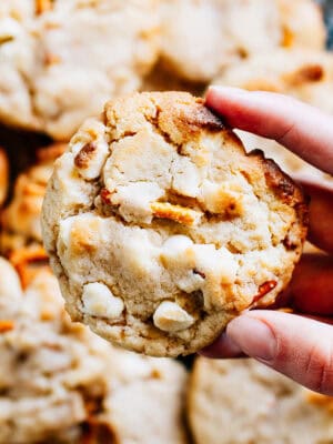 Someone holding a white trash cookie filled with white chocolate chips, toffee bits, and crunchy pretzels.