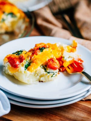 A piece of this potato quiche with its tender potato crust, spinach, pepper, and tomato center covered in eggs and topped with cheese. This is a fresh and filling breakfast.