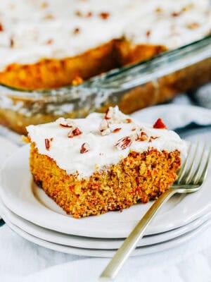 A close up photo of a cream cheese frosted carrot cake ready to be served on white plate.