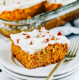 A close up photo of a cream cheese frosted carrot cake ready to be served on white plate.
