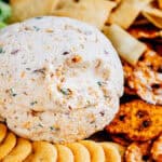 A party cheese ball of bacon and Ranch surrounded by crackers, crisps, chips, and celery.