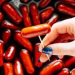 A BBQ little smokie on a toothpick being held above the slow cooker of little smokies.