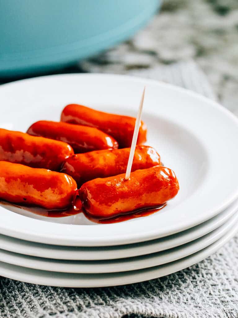 A plate of little smokies. One smokie has a toothpick in it.