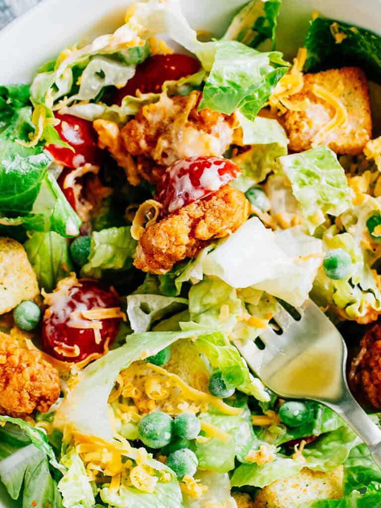 A forkful of lettuce, cherry tomato, and chicken from this supper yummy buffalo chicken salad.