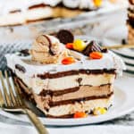 A slice of the best peanut butter ice cream sandwich cake that features layers of amazing ice cream sandwiches, creamy peanut butter, hot fudge topping, Reese's pieces, Reese's ice cream, and mini peanut butter cups.