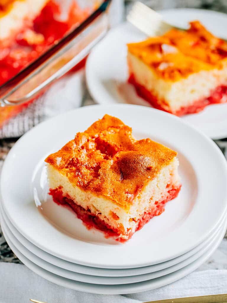 A Piece of white cake with mini marshmallows, strawberry jello, and rhubarb baked into it plated.