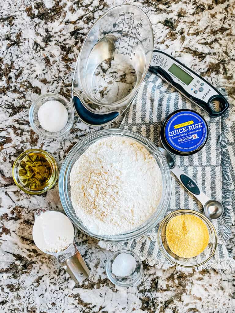Ingredients for an easy homemade English muffins recipe: warm water, flour, yeasts, sugar, salt, oil, and corn meal.