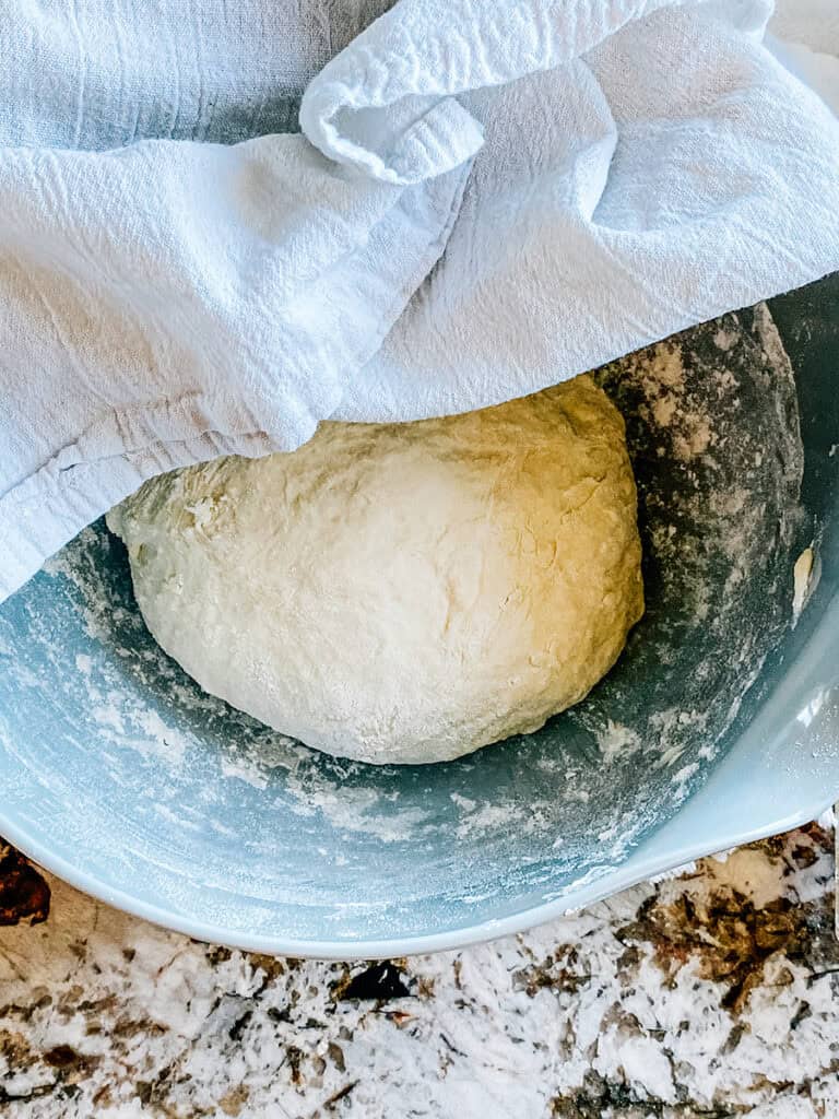 Towel covering muffin dough in bowl to rise for 1 hour in a warm spot.