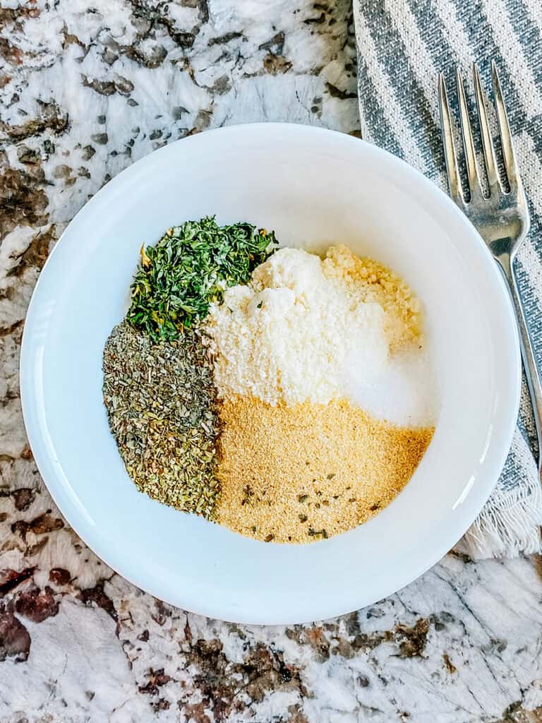 Dried basil, parsley, oregano, garlic powder, grated parmesan, and salt in a small bowl. The ingredients to a delicious Italian garlic seasoning that's perfect for pizza and breadsticks.