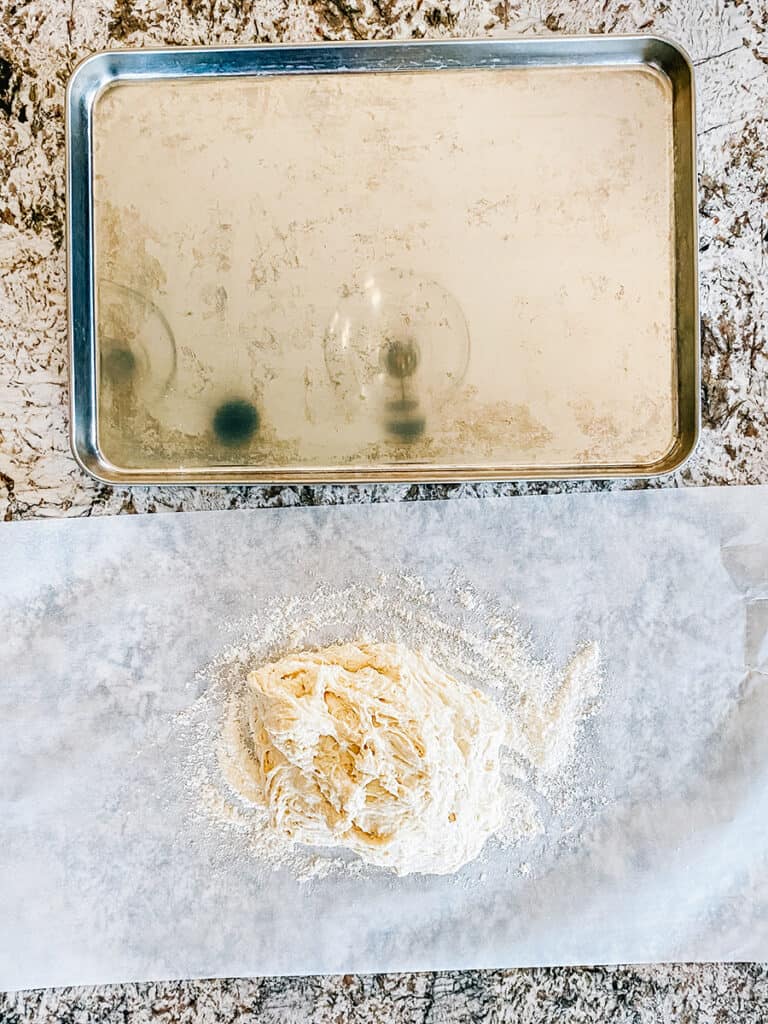 The sticky breadstick dough poured out onto a floured piece of parchment paper the size of a large rimmed baking sheet that we will use large to bake the homemade breadsticks.