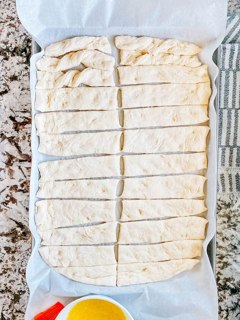 The parchment paper with the dough shapes on it pulled onto the large baking sheet to fit the cut breadsticks.