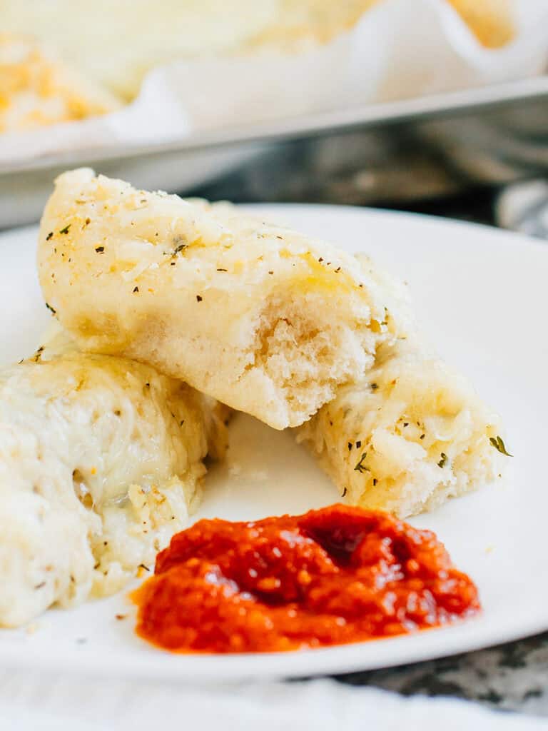 Soft cheesy breadsticks with a Italian seasoning plated next to marinara sauce.