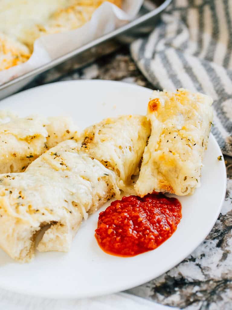 A plate of homemade breadsticks with cheese and Italian garlic seasoning.
