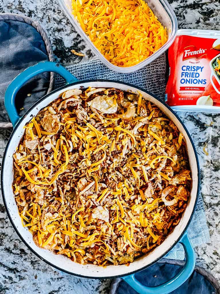The meat and potato casserole mixture topped with Frenchs fried onions and shredded cheddar cheese ready to be baked.
