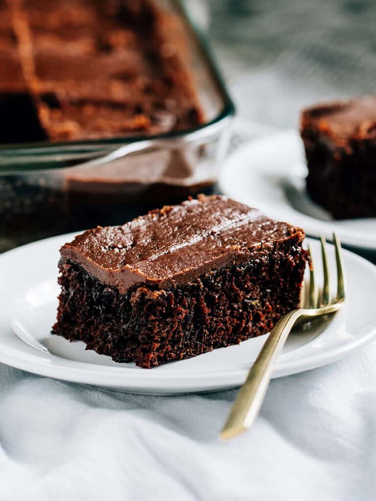 A piece of zucchini brownies with a chocolate frosting on a white plate.